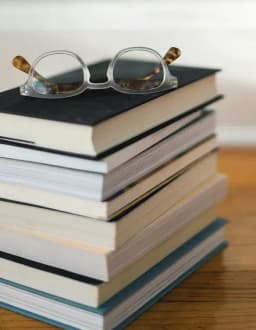 Stack of academic books with reading glasses on top