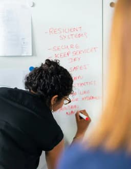 Person with curly hair writing on a whiteboard